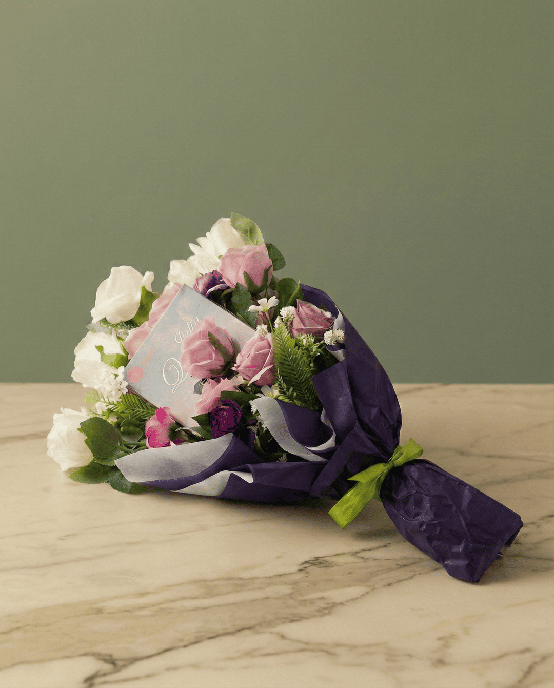 Bouquet letterario con tulipani gialli e viola avvolti in carta oro con un libro al centro su tavolo di marmo.