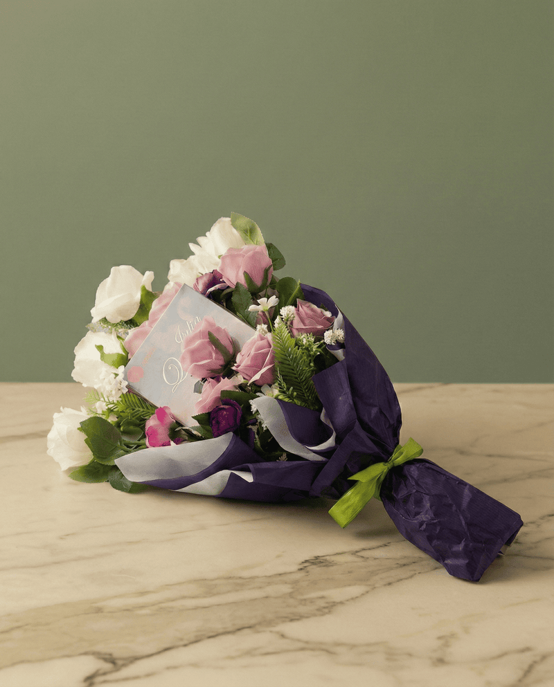 Bouquet letterario con tulipani gialli e viola avvolti in carta oro con un libro al centro su tavolo di marmo.