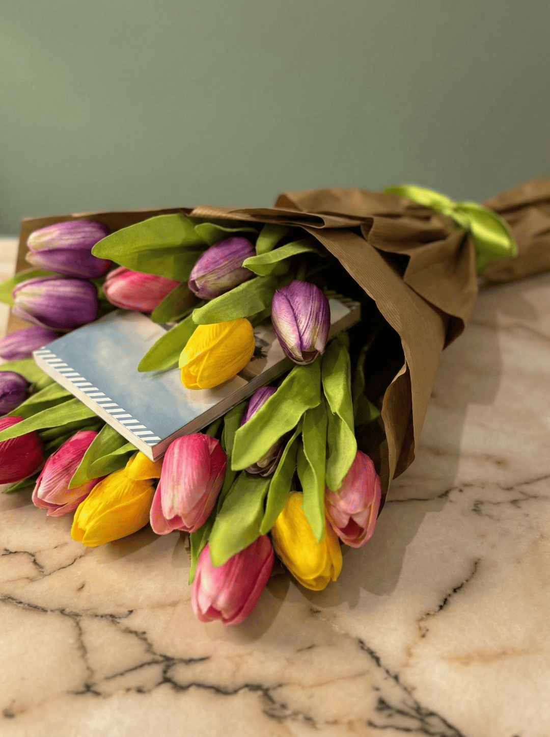 Dettaglio di tulipani gialli e viola che abbracciano un libro in una confezione regalo dorata.