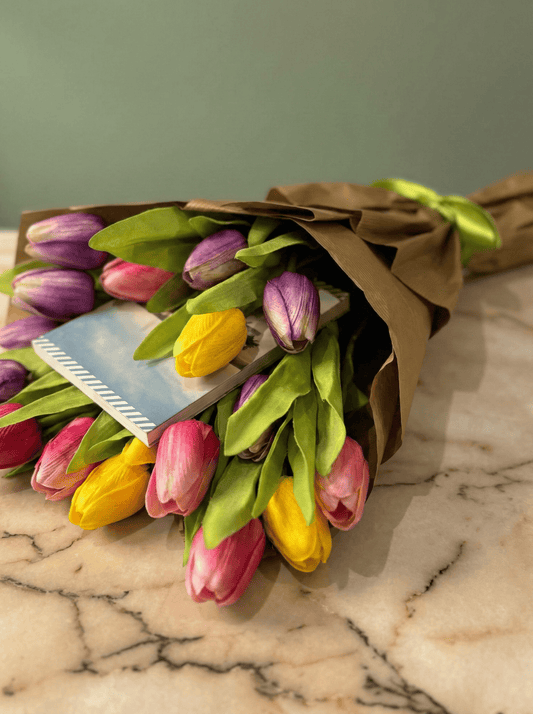 Dettaglio di tulipani gialli e viola che abbracciano un libro in una confezione regalo dorata.