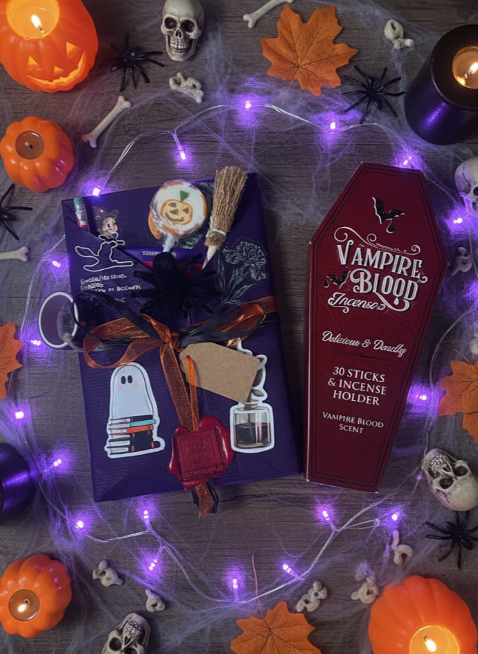 Confezioni regalo di libri a sorpresa per Halloween, ognuna contenente un lecca-lecca a zucca e altri piccoli gadget spettrali, adagiate tra foglie autunnali e candy corn.

